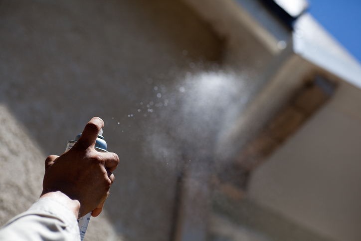 Pest control worker sprays wasp nest on a residential house.